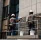 Dos operarios pintando la fachada de un edificio desde una plataforma